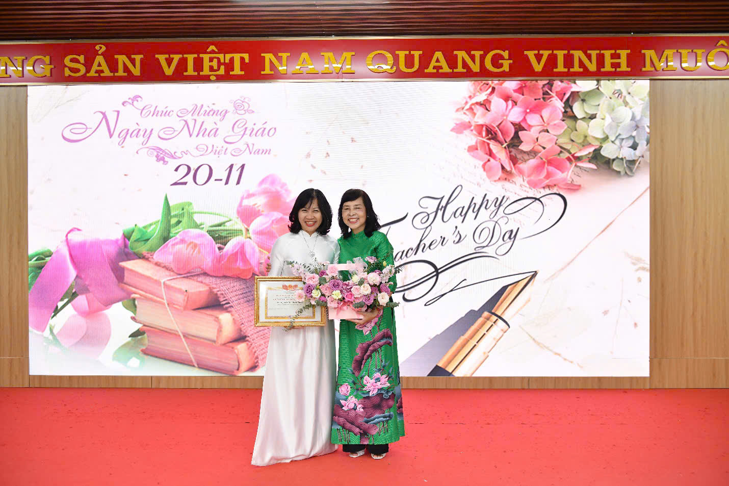 Two women holding flowers in front of a banner
Description automatically generated