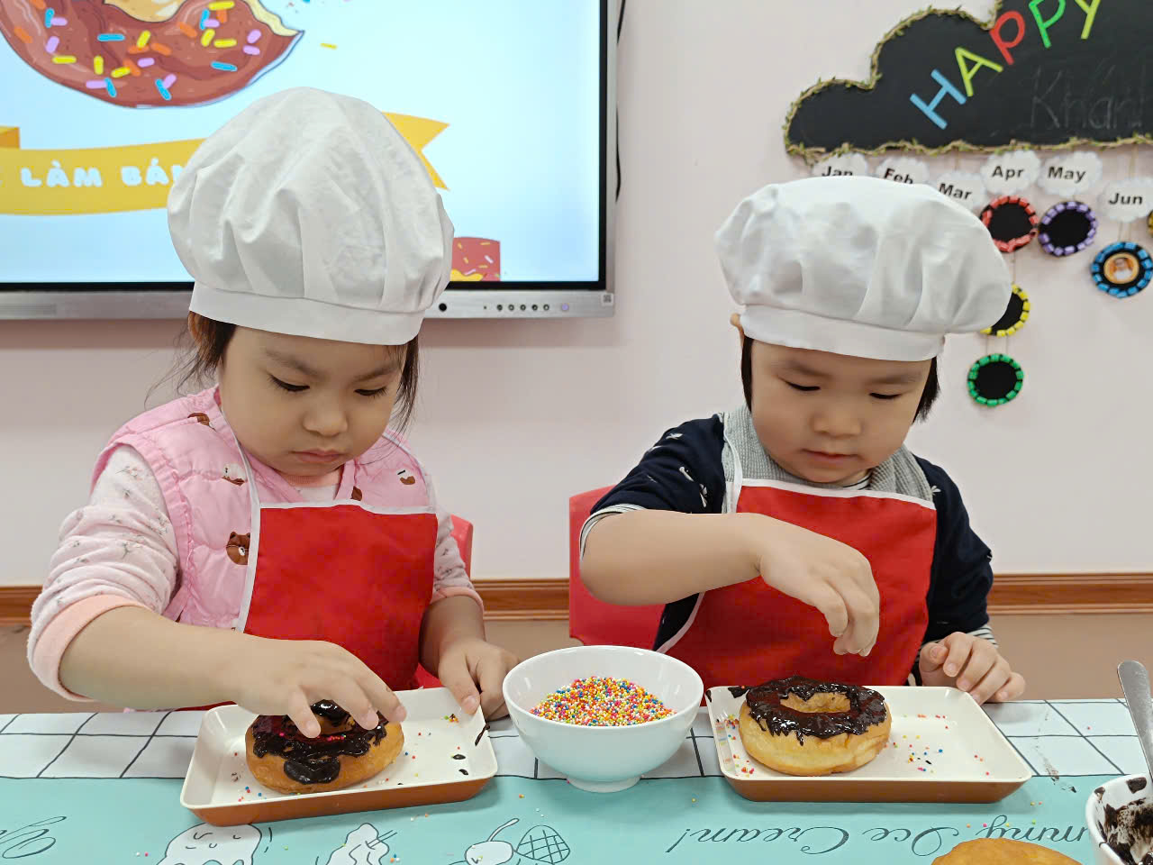 Two children wearing chef hats and red aprons
Description automatically generated