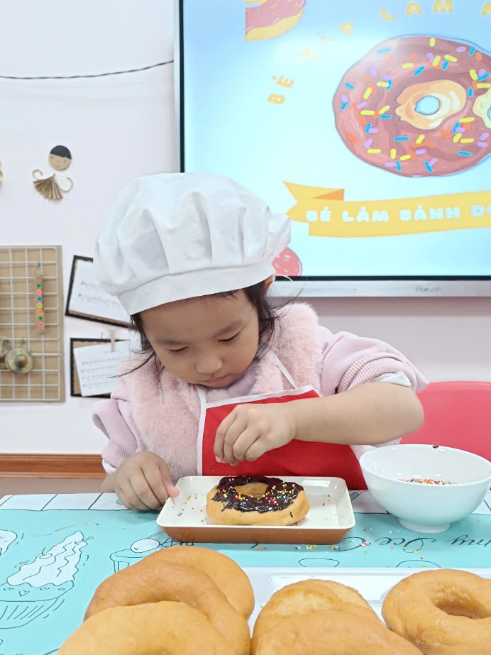 A child wearing a chef hat and holding a donut

Description automatically generated