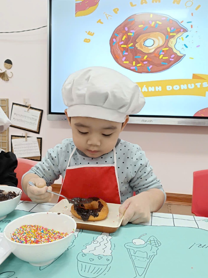 A child wearing a chef hat and apron eating a doughnut

Description automatically generated