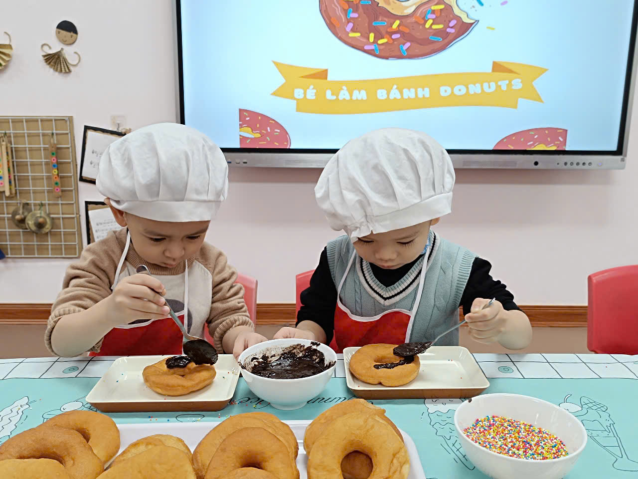 Two children wearing chef hats and eating doughnuts
Description automatically generated