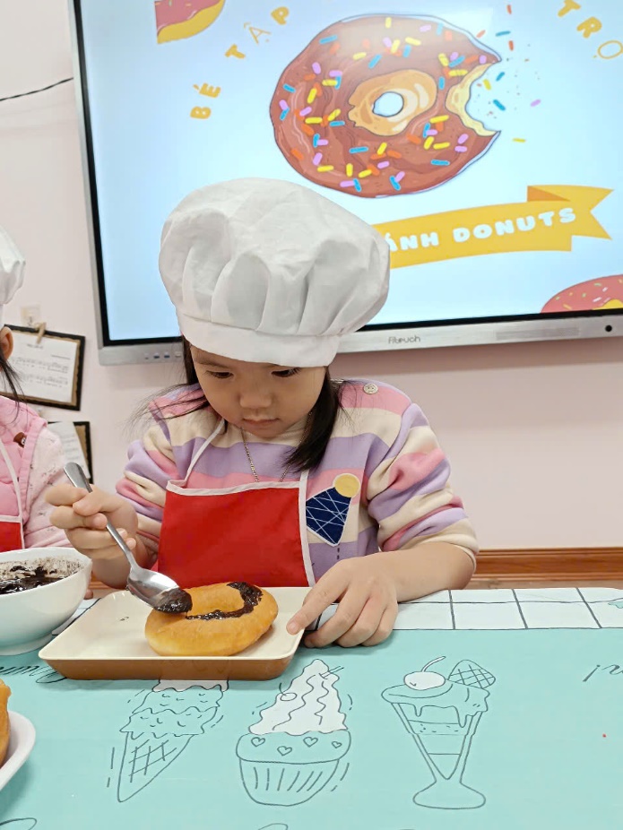 A child in chef hat and apron eating a doughnut

Description automatically generated